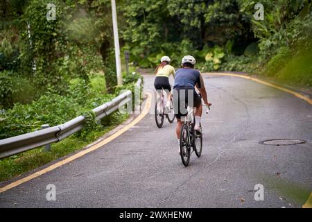 vue arrière de jeunes cyclistes de couple asiatique faisant du vélo sur la route rurale Banque D'Images