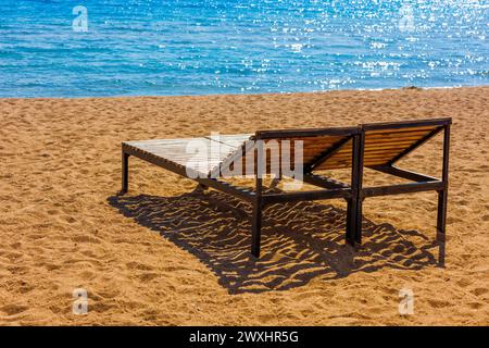 chaises longues extérieures vides sur la plage de sable près de l'eau bleue. Banque D'Images