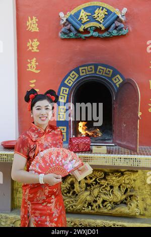 Une jolie femme asiatique brûle du papier et tient un ventilateur pour le culte au poêle brûlé en papier or et argent. Banque D'Images