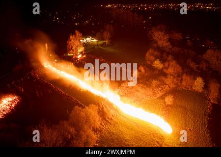 31 mars 2024, Rhénanie du Nord-Westphalie, Lügde : une roue de Pâques historique descend une colline en feu. Depuis 2018, la course de roues de Pâques de Lügde fait partie du patrimoine culturel immatériel allemand de l'UNESCO. Pendant le spectacle, d’énormes roues en bois bourrées de paille descendent une colline l’une après l’autre peu avant 21 heures. Photo : Christoph Reichwein/dpa Banque D'Images