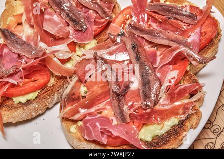 Toasts croquants garnés de délicieux jambon ibérique, de tranches de tomates juteuses, d'avocat crémeux et d'un filet d'huile d'olive vierge pour rehausser les saveurs. Une perf Banque D'Images