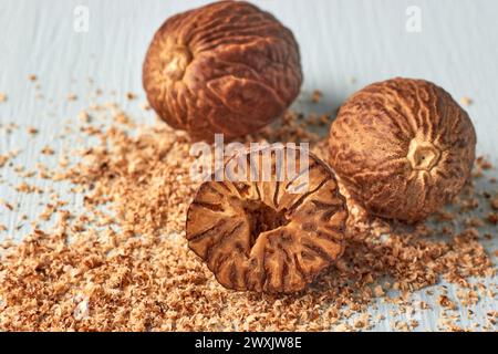 Trois noix de muscade texturées et poudre râpée sur un fond en bois clair. Épices pour la cuisson Banque D'Images