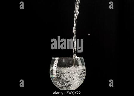 De l'eau tombant d'en haut dans un verre à vin. Isolé sur fond noir. Banque D'Images