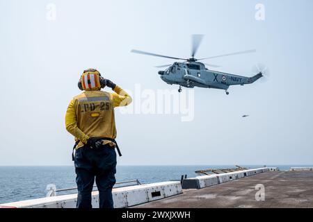 Avion Boatswain’s Mate (Handling) 3rd Class Michael Aguilar, originaire de Glendale, Californie, rend un hommage à un Sea King de la République de l’Inde UH-3H Sea King sur le pont d’envol du navire de transport amphibie USS Somerset (LPD 25) de classe San Antonio alors qu’il était en route dans la baie du Bengale, Mar. 28, 2024, lors de l'exercice Tiger TRIUMPH 2024. Tiger TRIUMPH est un exercice amphibie de trois services entre les États-Unis et l'Inde axé sur l'aide humanitaire et la préparation et l'interopérabilité des secours en cas de catastrophe. (Photo de l'US Navy par Evan Diaz, spécialiste des communications de masse, 2e classe) Banque D'Images