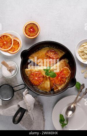 Crêpes à la sauce orange dans une casserole en fonte. Suzette traditionnelle en crêpe française à la sauce orange. Pose à plat, vue de dessus, espace de copie Banque D'Images