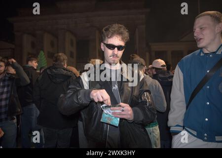 Berlin, du 31 mars au 1er avril 2024 - au milieu d'une atmosphère chargée d'anticipation et d'unité, la porte de Brandebourg à Berlin est apparue comme le point central d'un changement sociétal significatif dans la nuit menant aux premières heures du 1er avril 2024. Cet événement historique a marqué la progression de l'Allemagne vers une nouvelle ère dans la politique des drogues avec la légalisation partielle du cannabis pour usage récréatif, déclenchant une célébration collective parmi la foule réunie. La législation historique, entrée en vigueur le 1er avril, permet aux adultes allemands de posséder et de consommer légalement du cannabis, en fixant des limites de possession personnelle allant jusqu’à 25 gr Banque D'Images