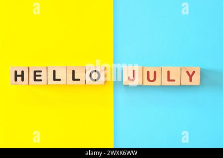 Bonjour mois de juillet concept. Typographie de blocs en bois en fond bleu vif et jaune. Banque D'Images
