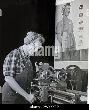 Cette photographie représente une jeune femme employée de l'ordonnance qui a reçu une formation d'usine de munitions par l'Administration nationale de la jeunesse alors qu'elle pose devant une affiche d'employée de l'ordonnance pendant la seconde Guerre mondiale CA. 1939-1943 Banque D'Images