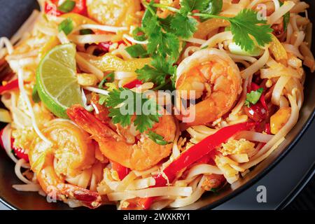 gros plan de pad thai, phad thai, nouilles de riz sautées avec crevettes, cacahuètes, œufs brouillés, germes de haricots, oignons verts, poivron rouge, citron vert, en noir Banque D'Images