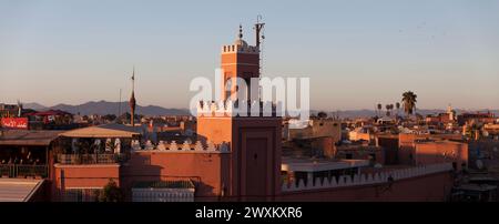 Marrakech, Maroc - janvier 28 2019 : minaret de la mosquée Kharbouch sur Jemaa el-Fnaa au coucher du soleil avec les montagnes de l'Atlas derrière. Banque D'Images