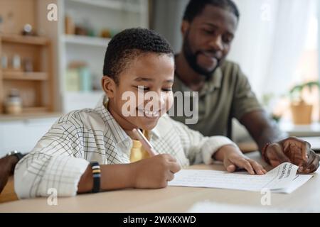 Portrait de garçon noir souriant faisant des devoirs à la table de cuisine avec le père aidant à copier l'espace Banque D'Images