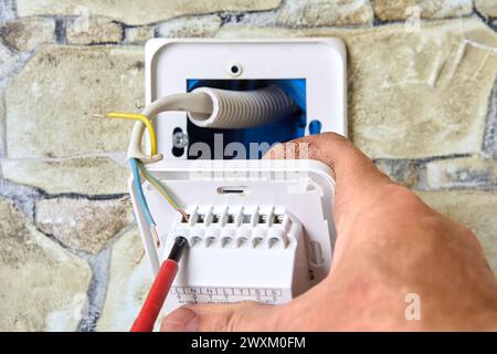 Câblage de la nouvelle prise électrique du thermostat dans le mur de pierre, électricien installation, connexion des fils de neutre et de terre sous tension, travail impliqué dans Banque D'Images