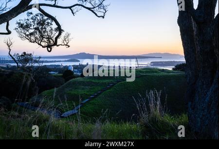 Aube au sommet du Mont Eden avec cratère volcanique au premier plan. Île de Rangitoto encadrée par des arbres Pohutukawa. Auckland. Banque D'Images