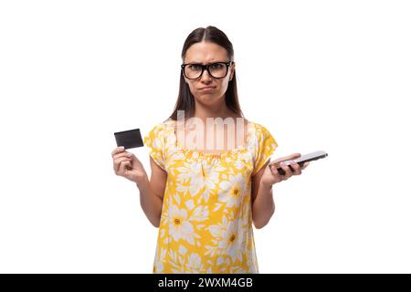 femme brune de 30 ans vêtue d'une tenue d'été est embarrassée et tient une carte en plastique dans sa main Banque D'Images
