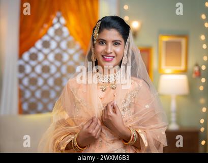 Heureuse femme musulmane indienne souriante debout avec dans des vêtements ethniques traditionnels en regardant la caméra à la maison - concept de fête du Ramadan, culture traditionnelle Banque D'Images