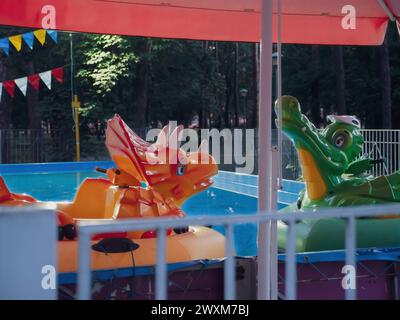 Dinosaure gonflable et alligator enfants chevauchant dans une piscine dans la soirée dans le parc d'attractions à Kiev, Ukraine. Banque D'Images