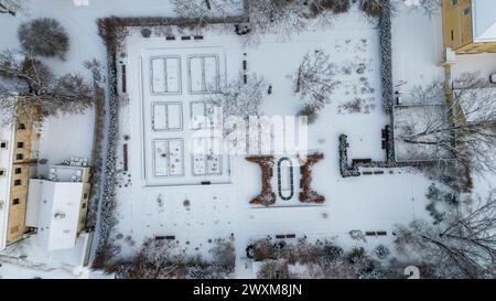 Photographie par drone d'un petit parc public avec une haie couverte de neige dans une ville pendant la journée nuageuse d'hiver Banque D'Images