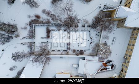 Photographie par drone d'un petit parc public avec une haie couverte de neige dans une ville pendant la journée nuageuse d'hiver Banque D'Images