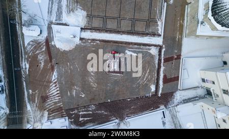 Photographie par drone d'un tracteur déneigant de la place publique pendant la journée nuageuse d'hiver Banque D'Images