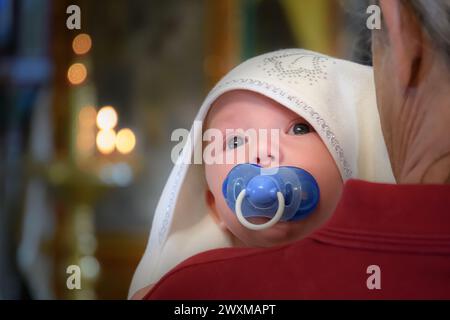 Moscou, Russie - 22 septembre 2018 : un enfant pleure avec une sucette dans les bras de son parrain lors d'une cérémonie de baptême dans le Chu orthodoxe russe Banque D'Images