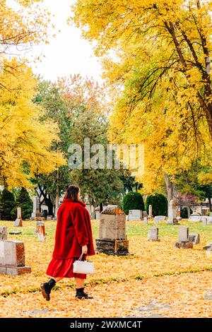 Femme en rouge marchant à travers le cimetière le jour d'automne Banque D'Images