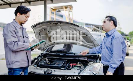 Un mécanicien discutant de réparation de voiture avec une autre personne dans un garage Banque D'Images