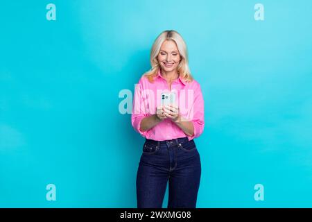 Portrait photo de jolie femme retraitée tenir le dispositif de chat tapant porter la tenue chic décontractée rose à la mode isolé sur fond de couleur cyan Banque D'Images