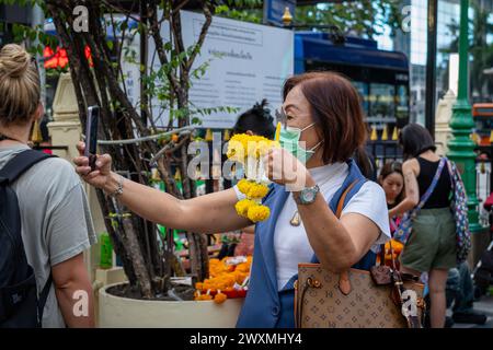 28 mars 2024, Bangkok, Thaïlande : une femme asiatique âgée est vue prendre un selfie avec sa guirlande de fleurs achetée pour une offrande, au sanctuaire Erawan, dans le centre-ville de Bangkok. Le sanctuaire Erawan, dédié au Dieu Brahma, est un site vénéré où les visiteurs de Thaïlande et du monde entier offrent de l'encens, des guirlandes, des fruits et des statues d'éléphants, espérant que leurs souhaits se réaliseront. En outre, le sanctuaire contribue à des causes caritatives, en fournissant un soutien aux hôpitaux et aux organisations dans toute la Thaïlande. (Crédit image : © Nathalie Jamois/SOPA images via ZUMA Press Wire) USAGE ÉDITORIAL SEULEMENT! Non Banque D'Images