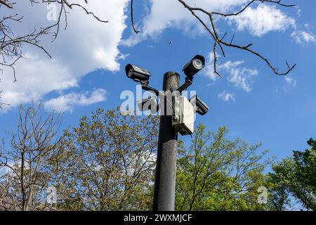 Caméras de surveillance montées sur un poteau surveillant un parc public à Bucarest, en Roumanie, pendant une journée ensoleillée avec un ciel bleu et des nuages dispersés Banque D'Images