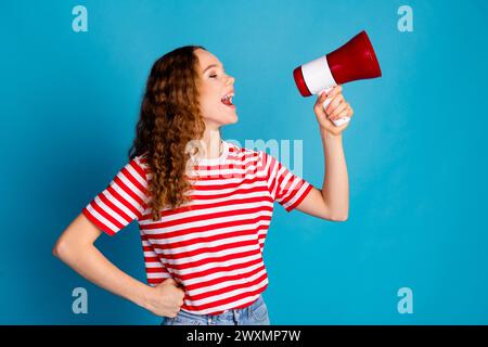 Photo d'une femme optimiste avec un t-shirt rayé habillé ondulé annonçant la vente dans un haut-parleur isolé sur fond de couleur bleue Banque D'Images