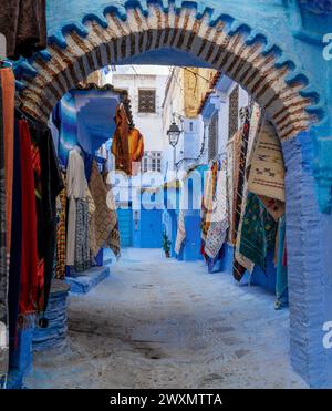 Chefchaouen, Maroc - 2 mars 2024 : porte voûtée avec des tapis colorés sur le mur dans la ville bleue historique de Chefchaouen, dans le nord du Maroc Banque D'Images