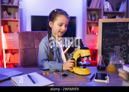 Petite fille en chemise denim apprenant la science le soir à la maison. Banque D'Images