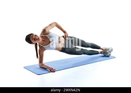 Portrait dynamique de la jeune femme athlète se tient en planche latérale et tient la main sur la hanche sur fond blanc de studio. Banque D'Images