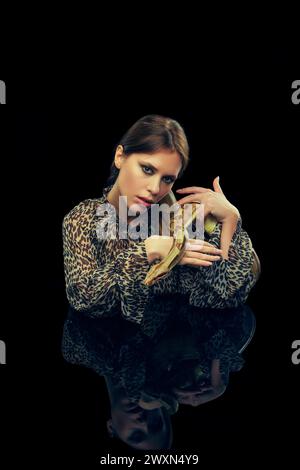 Portrait de jeune femme avec le maquillage, en chemisier imprimé animal posant avec serpent sur fond noir de studio. Banque D'Images