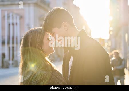Close up portrait of a beautiful young caucasian couple kissing contre coucher de la lumière tout en recherchant à l'extérieur. Banque D'Images