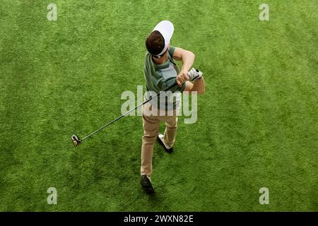 Vue sous un angle supérieur d'un golfeur habile en tenue décontractée frappant une balle de golf sur l'herbe verte du fairway. Concept de loisirs, jeux de sport. Banque D'Images