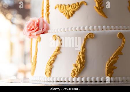 un élégant gâteau de mariage présente des volutes d'or complexes et une rose fondante rose unique, un véritable chef-d'œuvre de confiserie Banque D'Images