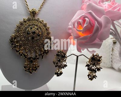 Un vase blanc tenant des fleurs violettes et un collier avec un pendentif Banque D'Images