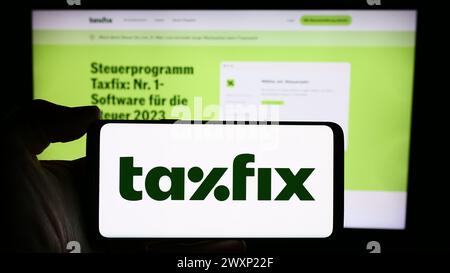 Personne tenant le téléphone portable avec le logo de la société allemande de logiciels fiscaux Taxfix se en face de la page Web de l'entreprise. Concentrez-vous sur l'affichage du téléphone. Banque D'Images