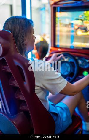 Femme jouant au jeu de simulateur de course dans le parc à thème. Banque D'Images