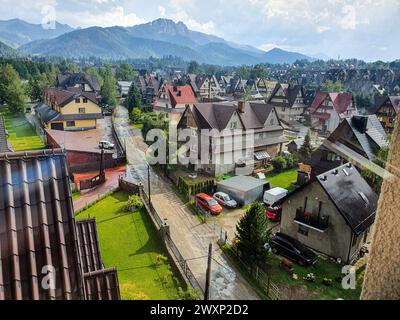 Vue partielle de la ville de Zakopane, à l'intérieur de la Pologne, avec ses maisons aux toits triangulaires, herbe dans le jardin, montagnes en arrière-plan. Banque D'Images
