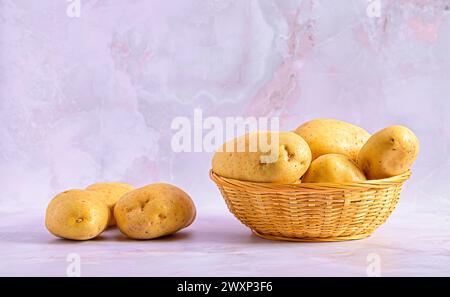 Pommes de terre fraîches dans un panier en osier sur une surface en marbre clair Banque D'Images