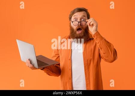 Stupéfait chevelu barbu tient un ordinateur portable regardant la caméra, le studio Banque D'Images