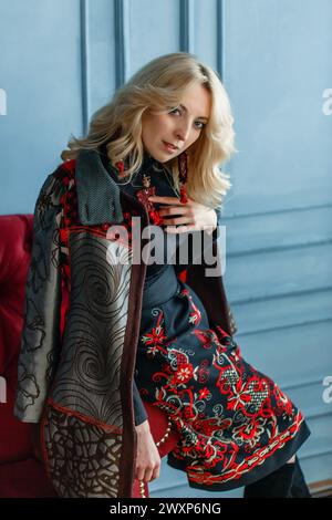 Une femme portant une robe noire est assise sur un canapé rouge vif. Banque D'Images