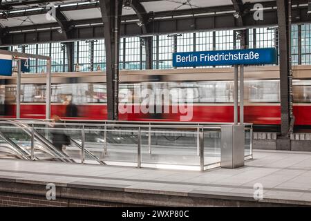 Panneaux d'affichage avec le nom de la gare Berlin Friedrichstrasse. Ancienne gare vintage, avec train de passagers à double étage visible en mouvement PA Banque D'Images