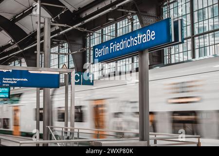 Panneaux d'affichage avec le nom de la gare Berlin Friedrichstrasse. Ancienne gare vintage, avec train de passagers à double étage visible en mouvement PA Banque D'Images