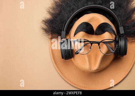 Visage de l'homme fait de cheveux artificiels, sourcils, lunettes et chapeau sur fond beige, vue de dessus. Espace pour le texte Banque D'Images