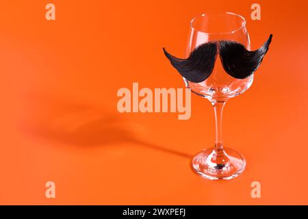 Visage de l'homme fait de moustache artificielle et verre de vin sur fond orange. Espace pour le texte Banque D'Images