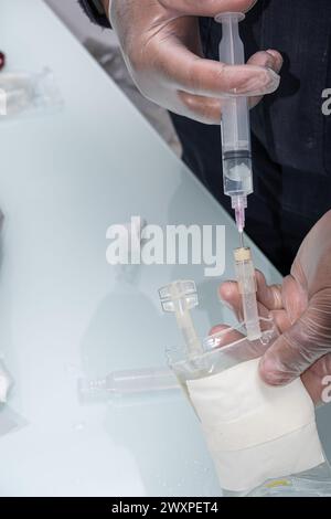 Infirmière avec des gants de protection, injectant un anti-inflammatoire dans le sac avec du sérum. Banque D'Images