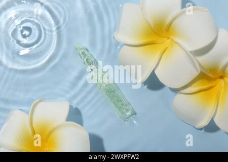 Ampoule de soin de la peau et belles fleurs de plumeria dans l'eau sur fond bleu clair, pose plate Banque D'Images